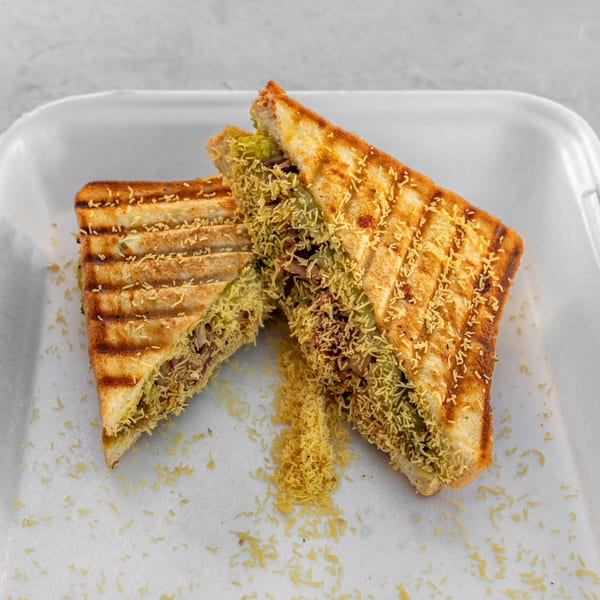 Two grilled Bombay sandwiches, cut diagonally, filled with savory ingredients and topped with sev.