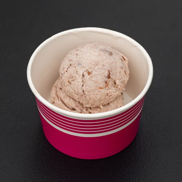 Two scoops of brown ice cream with specks, served in a pink and white striped cup.