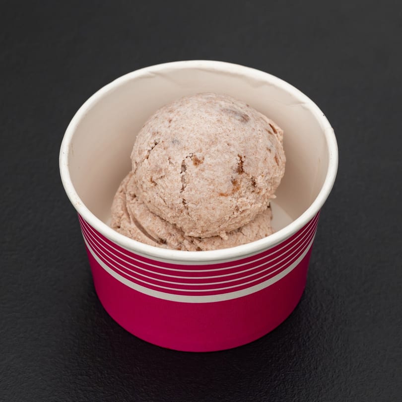 Two scoops of brown ice cream with specks, served in a pink and white striped cup.