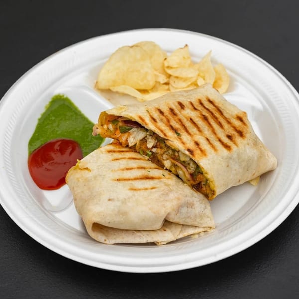 Two grilled Indian wraps, one cut open, with green chutney, ketchup, and chips on a white plate.