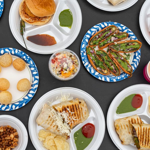 An overhead view of various Indian street food dishes, including vada pav, pani puri, and wraps.