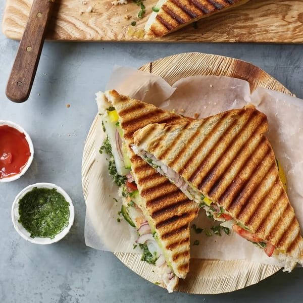 Grilled Bombay street food sandwich with vegetables and sauces on a wooden plate.