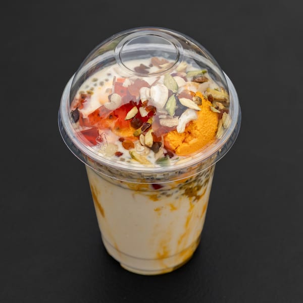 A clear plastic cup of Indian falooda, topped with nuts, dried fruit, and orange ice cream.