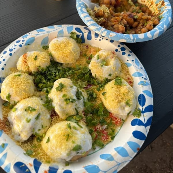 A plate of Dahi Puri topped with yogurt, sev, and cilantro, with a bowl of chana chaat.